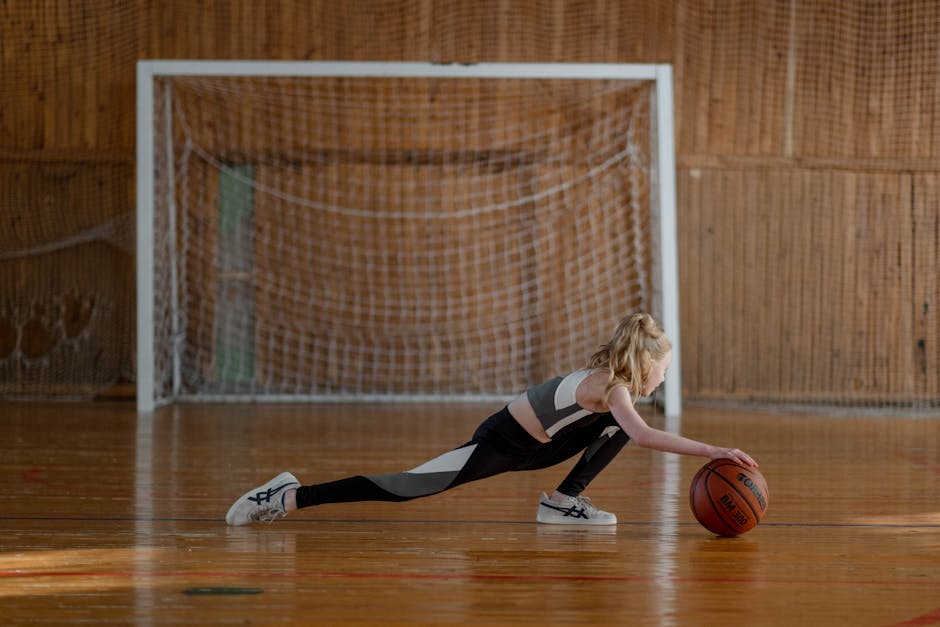 warm-up routines for youth sports practice - A young girl stretching with a basketball in an indoor sports hall.