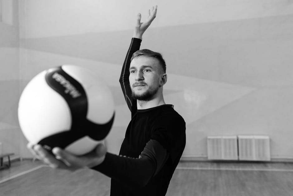 youth volleyball skills - Black and white photo of a male volleyball player poised with the ball indoors.
