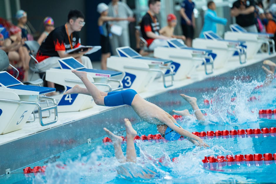 Young swimmers dive into a pool at the start of a competitive race, showcasing athletic prowess and teamwork.