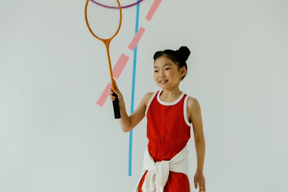 youth sports news - Smiling young girl playing badminton indoors, showcasing athletic joy.