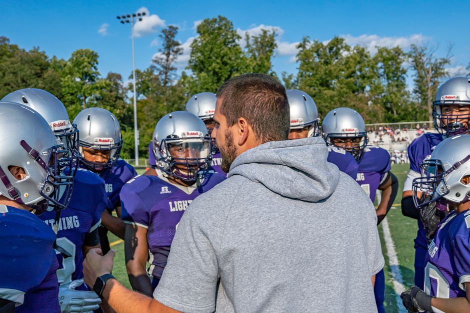 Boys Participation Hits 42%, Girls Gap Opens at 8, Overtime Lands Eldridge Raise, U.S. Bank Backs NFL FLAG: 15 Must-Know Youth Sports Stories (October 4, 2026) 2 youth sports news - A coach leads a football team huddle during a game outdoors in Columbia.